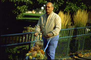 An older adult male human pushes a youngster in a stroller.